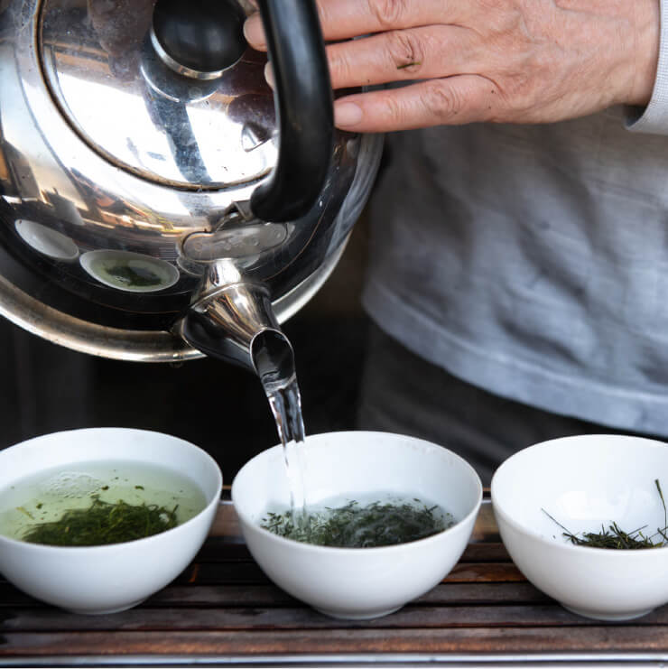 コップに入ったお茶の葉にやかんでお湯を入れている写真